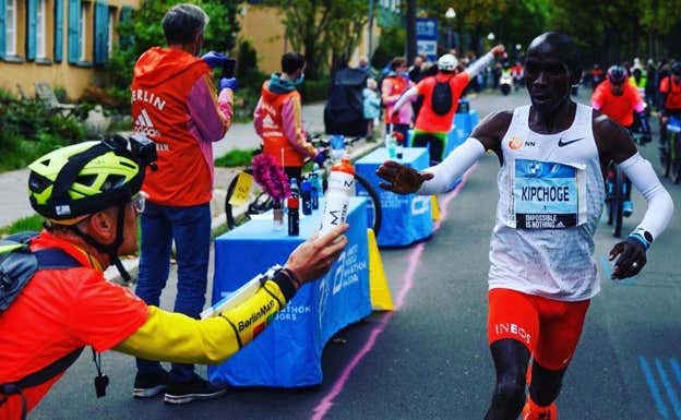 Claus entrega un bidón a Kipchoge en la maratón de 2022.  CLAUSS-HENNING SCHULKE