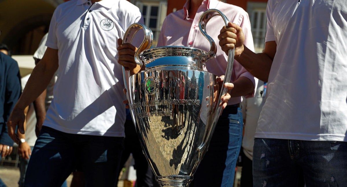 Una copa de la Champions League sujetada por dos aficionados.