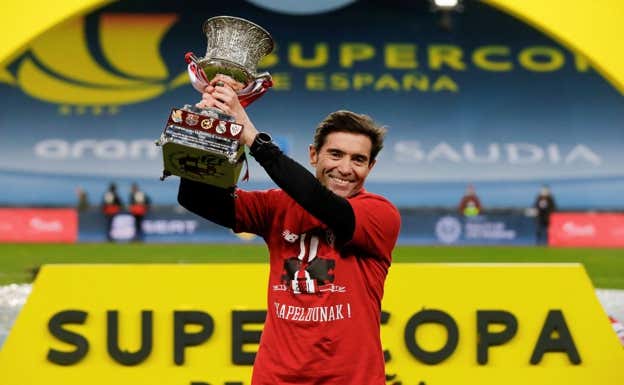 Marcelino García Toral, entrenador del Athletic en 2021, alza la copa con la lona detrás.  EFE/Pablo García
